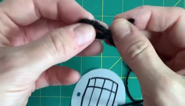 Cut your wool or string into two pieces and thread each piece through the holes, tying a knot at the end.